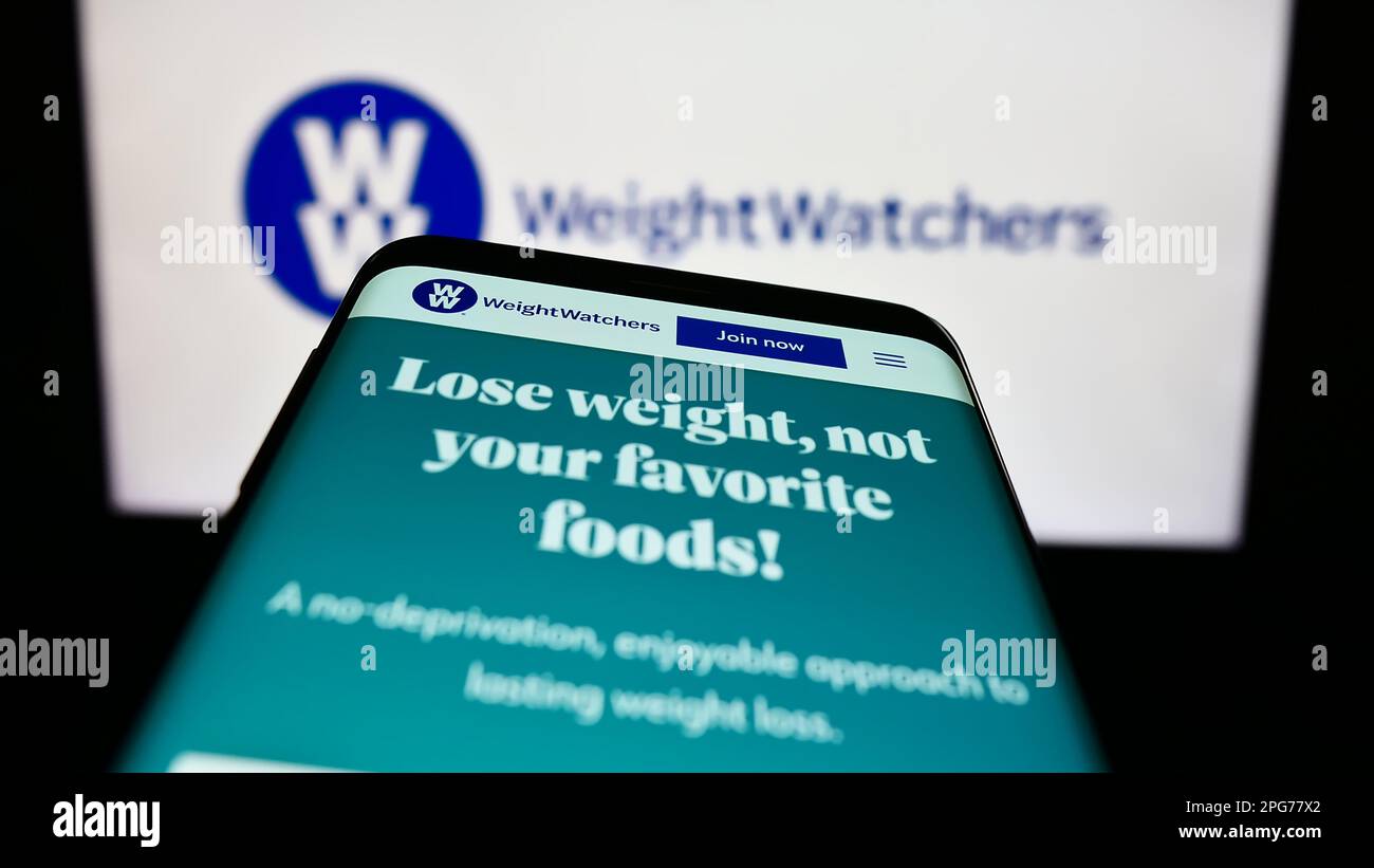 Smartphone avec le site Web de WW International Inc (Weight Watchers) à  l'écran devant le logo de l'entreprise. Faites la mise au point dans le  coin supérieur gauche de l'écran du téléphone