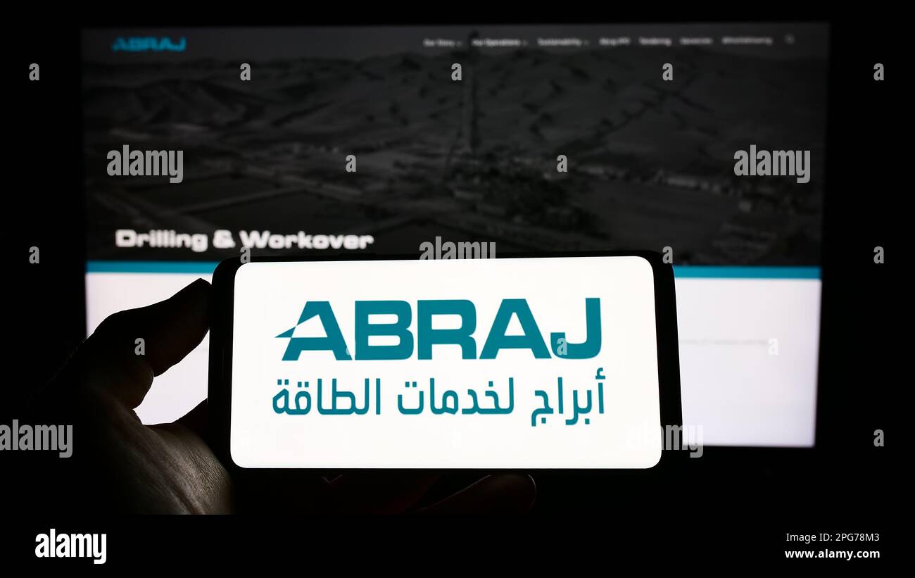 Personne tenant un téléphone portable avec le logo de la compagnie pétrolière omanaise Abraj Energy Services à l'écran en face de la page Web d'affaires. Mise au point sur l'affichage du téléphone. Banque D'Images