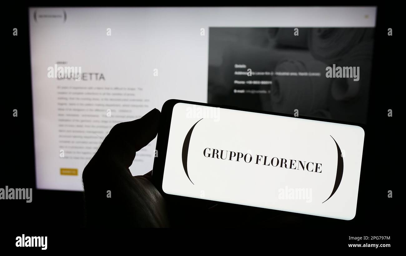 Personne tenant un téléphone portable avec le logo de la société italienne de mode Gruppo Florence spa à l'écran en face de la page web d'affaires. Mise au point sur l'affichage du téléphone. Banque D'Images