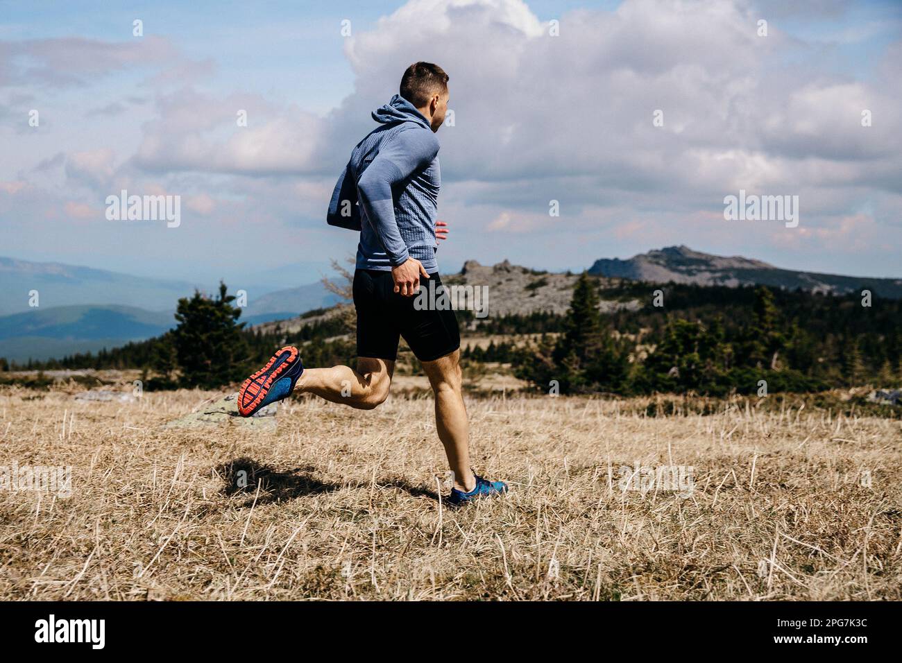 homme coureur piste de montagne sur herbe sèche, vue latérale, chemise à manches longues bleue et collants noirs, photo de sport Banque D'Images
