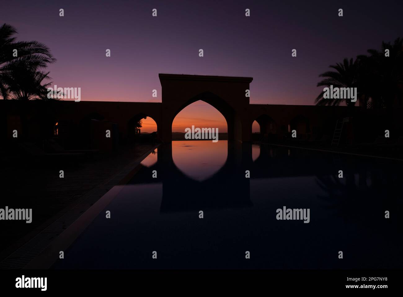 Lever de soleil au-delà d'une arcade au bout d'une piscine à débordement. A l'hôtel Tilal Liwa Desert Resort près d'Abu Dhabi, eau, United Arab EMI Banque D'Images