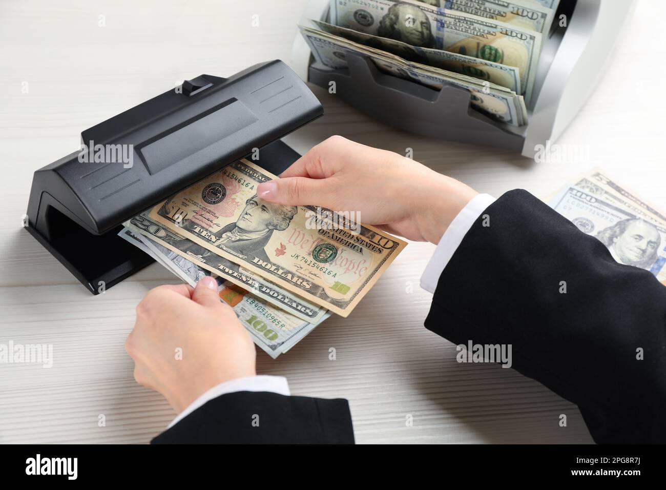 Femme vérifiant des billets en dollars avec détecteur de devises sur table en bois blanc, gros plan. Appareil d'examen de l'argent Banque D'Images