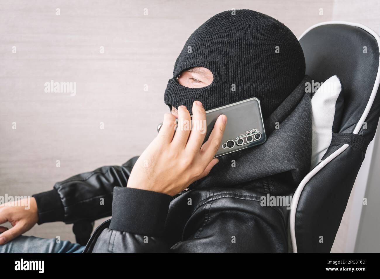 Le voleur fait un geste de téléphone. Le concept de terrorisme et de fraude par téléphone. Un homme masqué passe un appel téléphonique. Banque D'Images