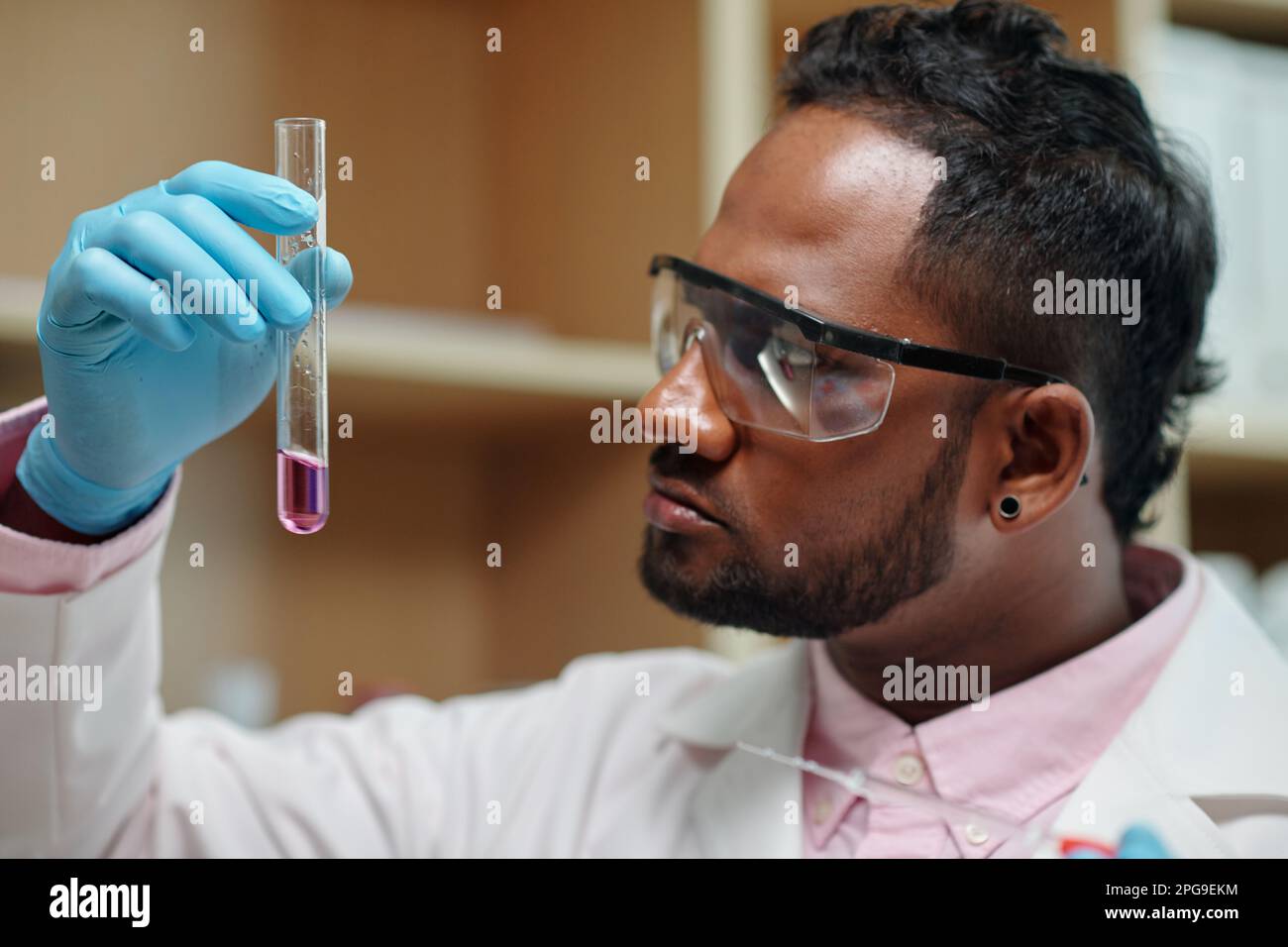 Jeune chimiste en gants, lunettes et blouse de laboratoire regardant un  flacon contenant une substance liquide tout en tudiant ses  caractristiques Photo Stock - Alamy