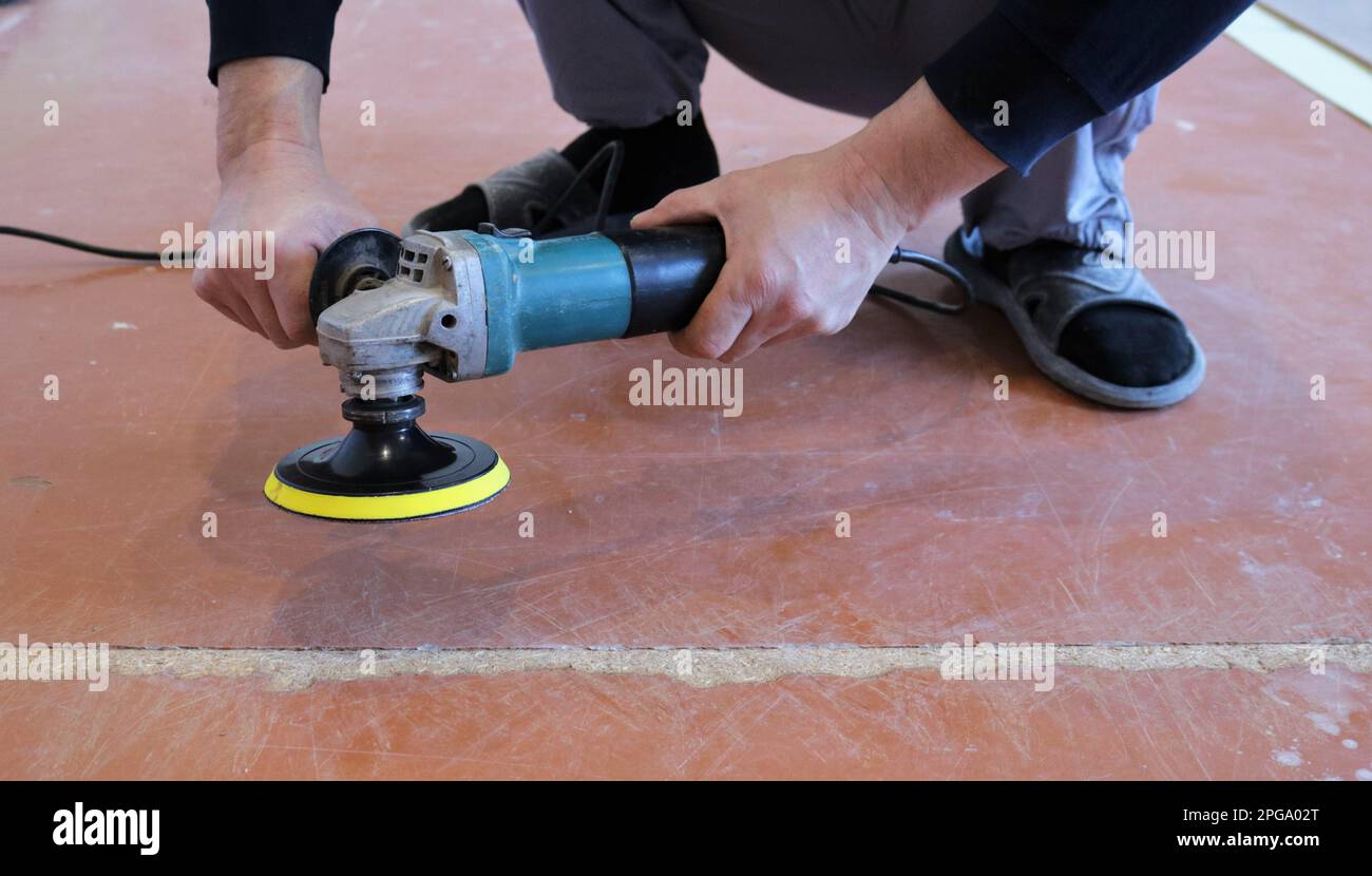 buse ronde jaune émeri sur une meuleuse dans les mains d'une personne en cours de meulage d'un vieux plancher brun en bois dans la zone de couture Banque D'Images