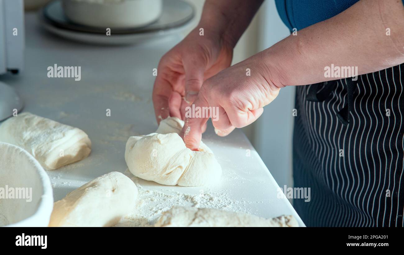 Un chef cuisinier fait du pain maison sur une table blanche. Chef étirant et pliant la pâte à pain sur une table blanche avec vue latérale sur la farine saupoudrée. Banque D'Images