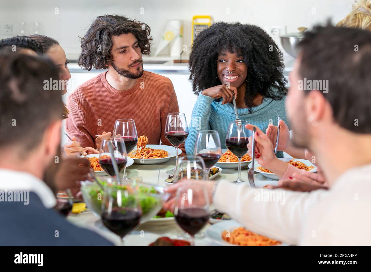 Les amis multiethniques mangent des spaghetti à la sauce tomate dans la cuisine d'un appartement partagé Banque D'Images