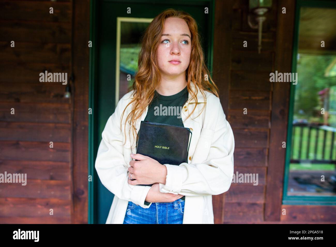 Une jeune femme avec une expression sérieuse se tient à l'extérieur, tenant la Sainte Bible Banque D'Images