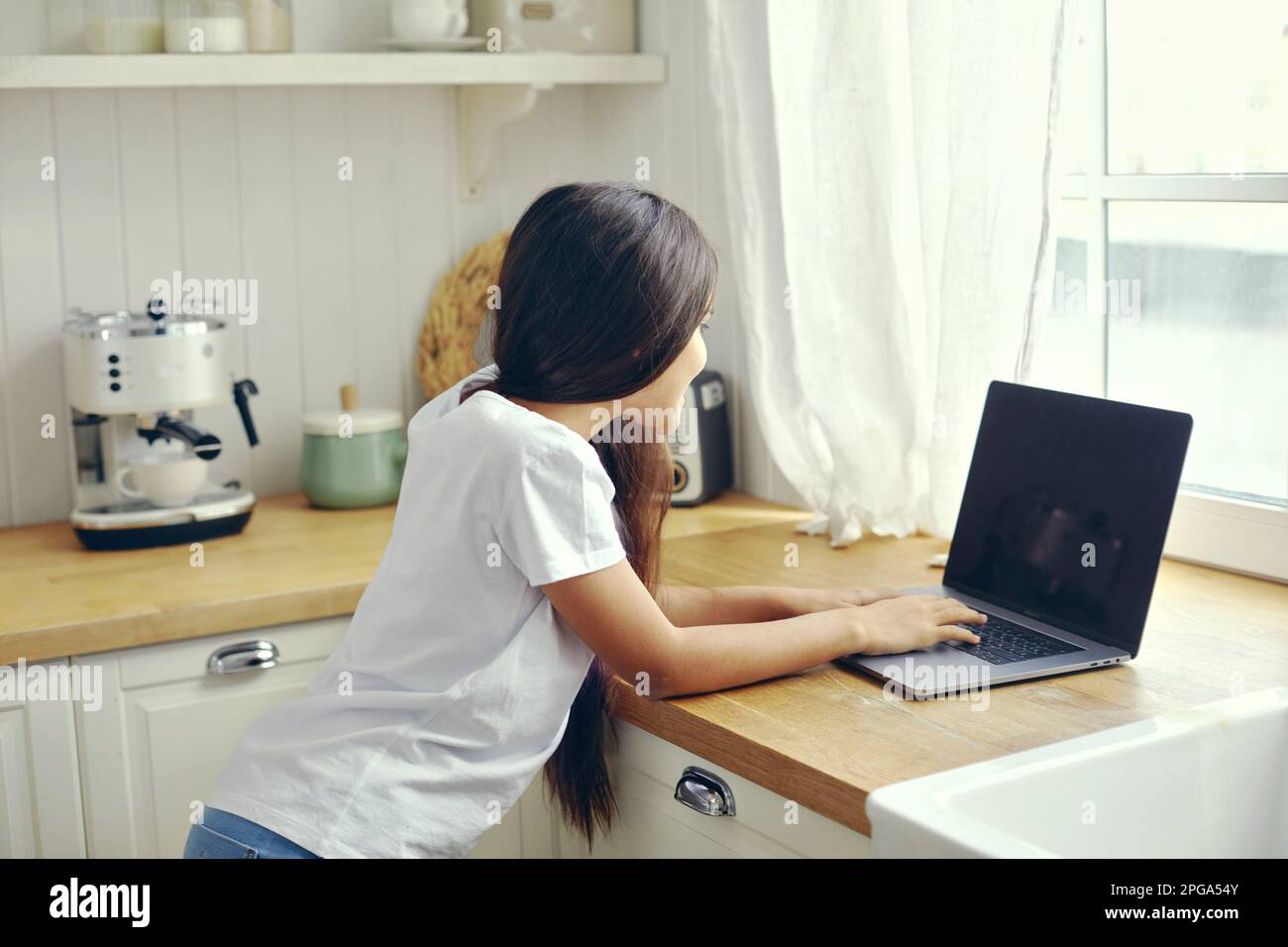 12s fille utiliser le stand d'ordinateur portable dans la cuisine, taper sur le clavier, rechercher des informations, faire la tâche, étudier en ligne, discuter avec des amis via les réseaux sociaux ou m Banque D'Images