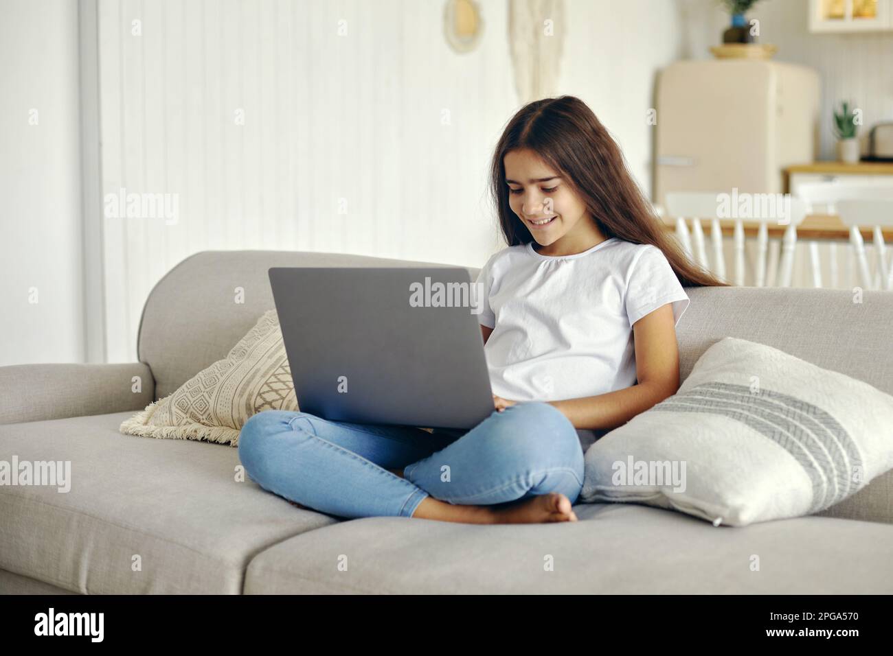Beautiful12s girl utiliser l'ordinateur portable s'asseoir sur le canapé dans le salon confortable, taper sur le clavier, rechercher des informations, faire la tâche, étudier en ligne, discuter avec un ami Banque D'Images