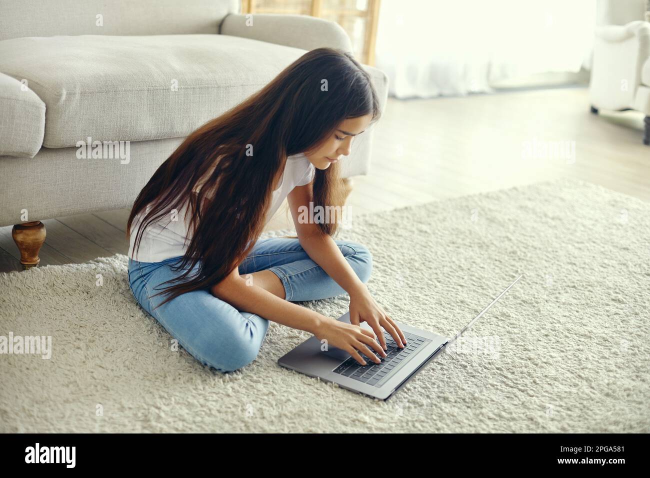 Mignon préteen 12s fille utiliser ordinateur portable s'asseoir sur le sol dans le salon confortable, taper sur le clavier, rechercher des informations, faire la tâche, étudier en ligne, discuter avec f Banque D'Images