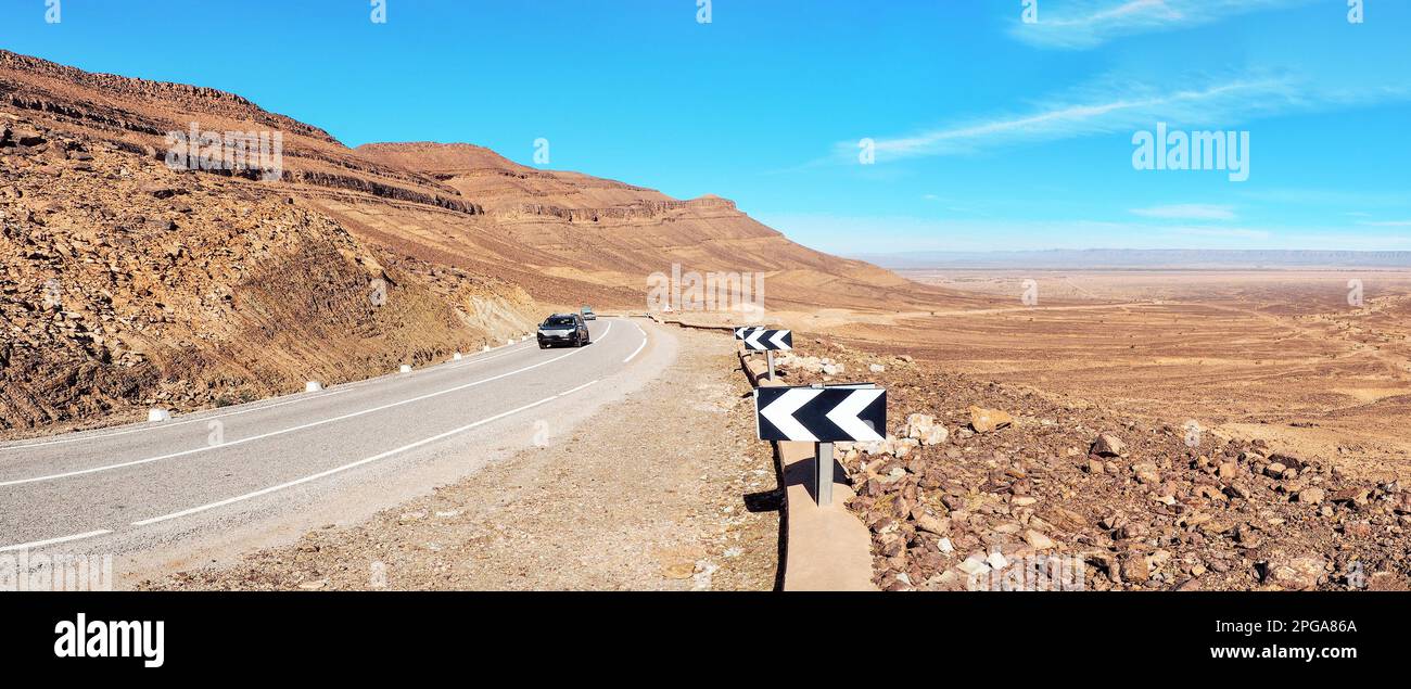 Courbe sur route asphaltée, petites montagnes de l'Atlas et buissons bas des deux côtés, ciel clair au-dessus - paysage typique dans le sud du Maroc Banque D'Images