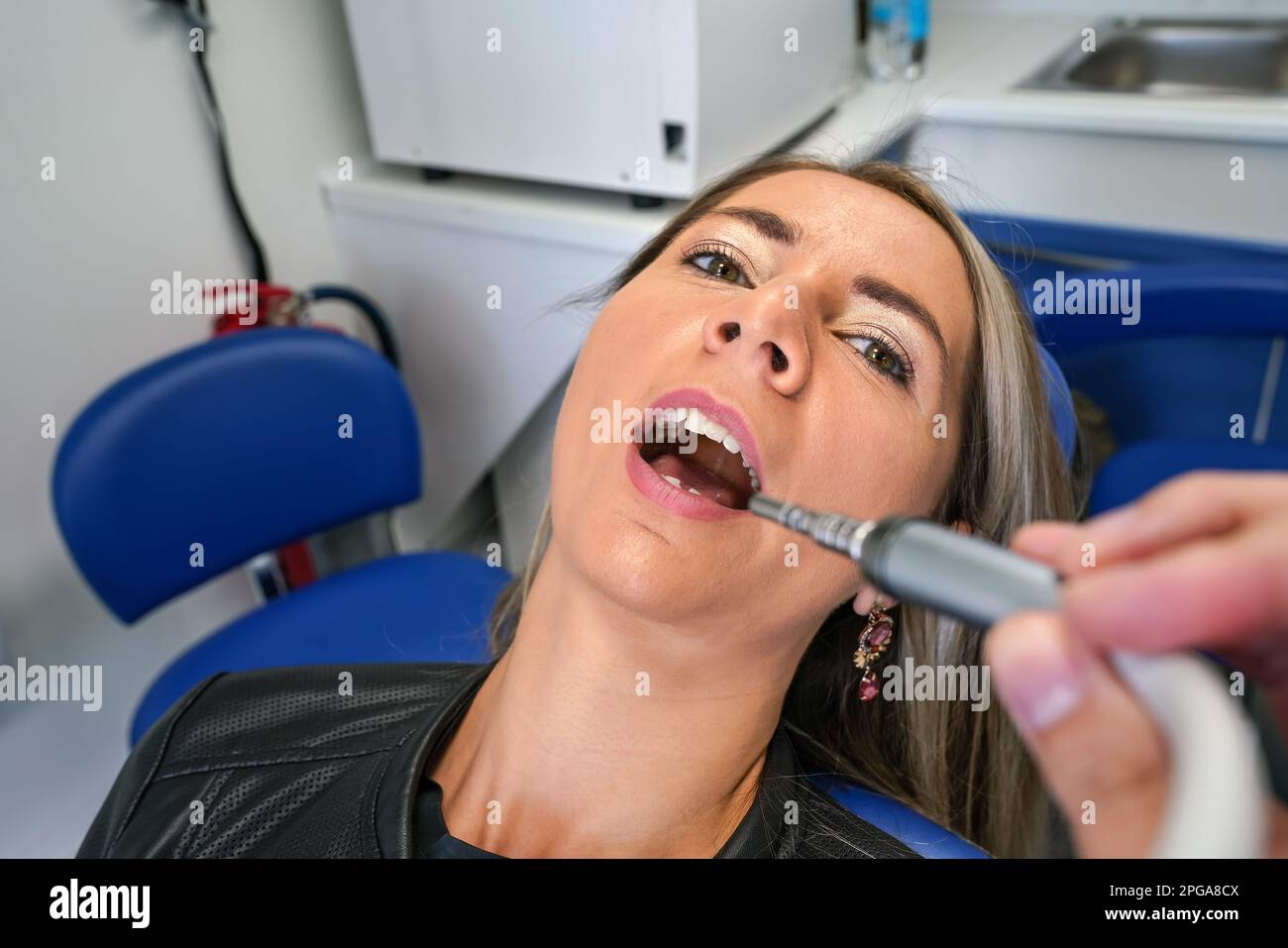 Jeune femme posant avec sa bouche ouverte à la chaise de dentiste, outil dentaire près de ses dents, vue de la première personne Banque D'Images