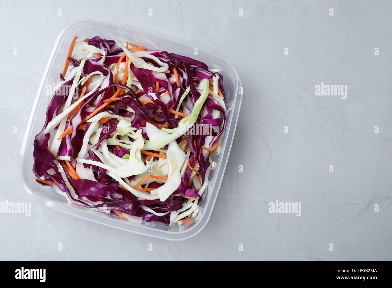 Salade de chou frais avec carotte déchiquetée dans un récipient en plastique sur une table légère, vue du dessus. Espace pour le texte Banque D'Images