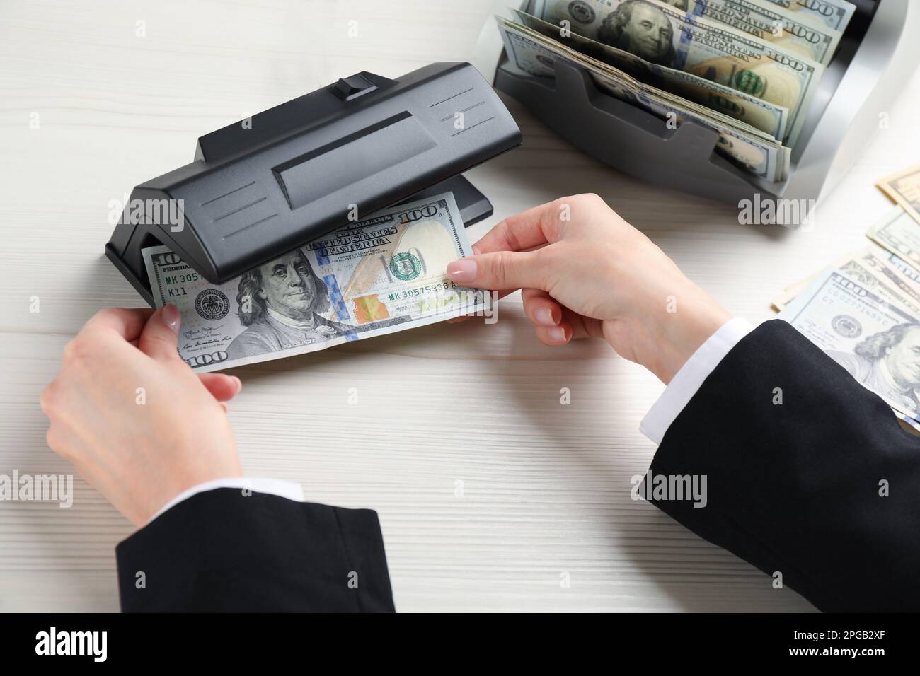 Femme vérifiant le billet de dollar avec détecteur de devises sur une table en bois blanc, au-dessus de la vue. Appareil d'examen de l'argent Banque D'Images
