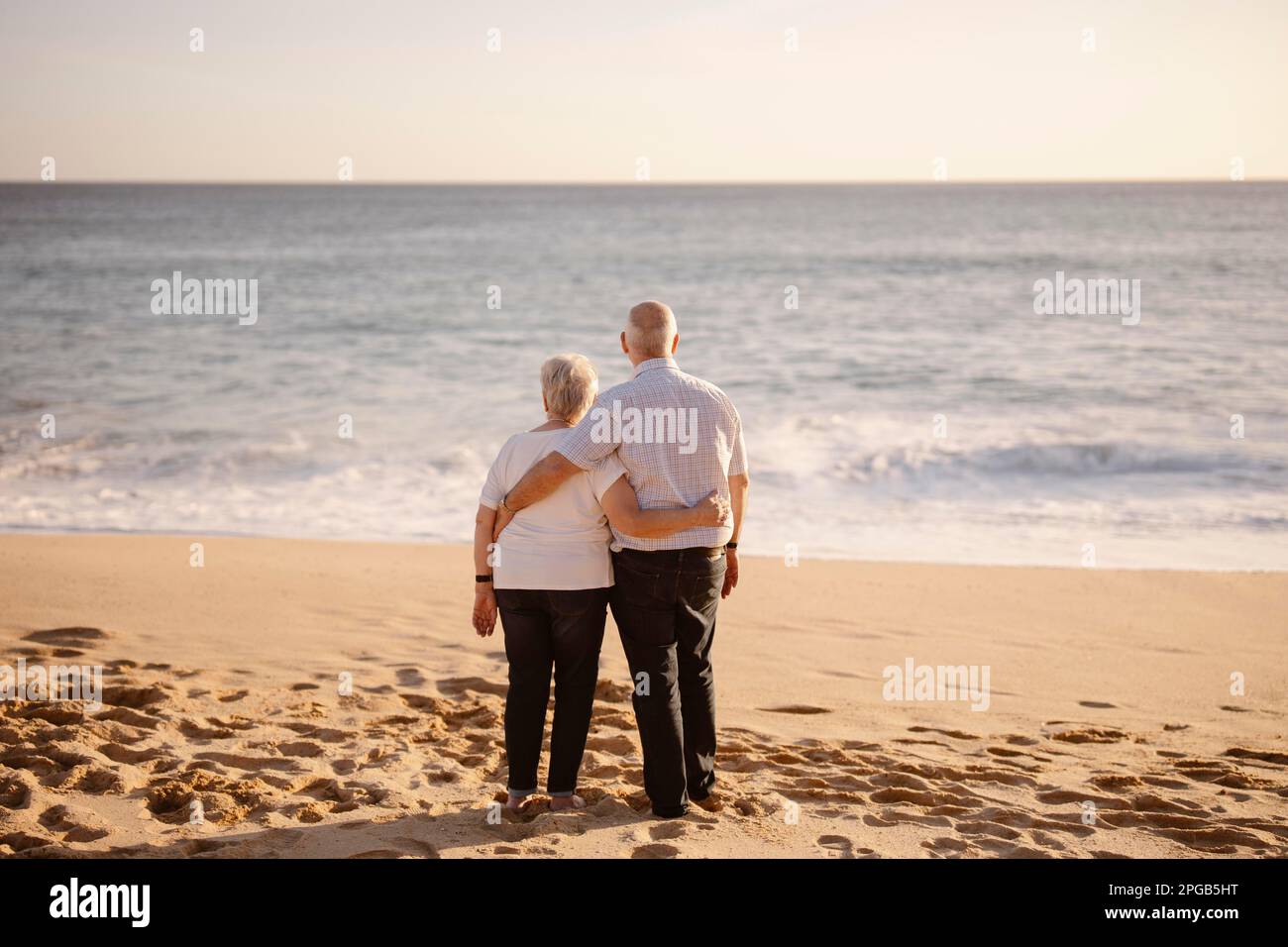 Couple âgé se embrassant sur la plage vue de leur dos Banque D'Images