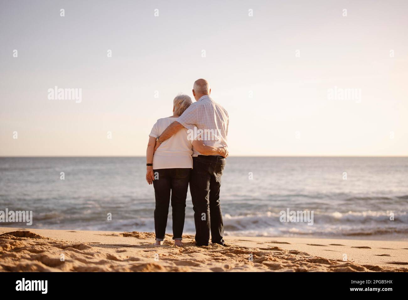 Couple âgé se embrassant sur la plage vue de leur dos Banque D'Images