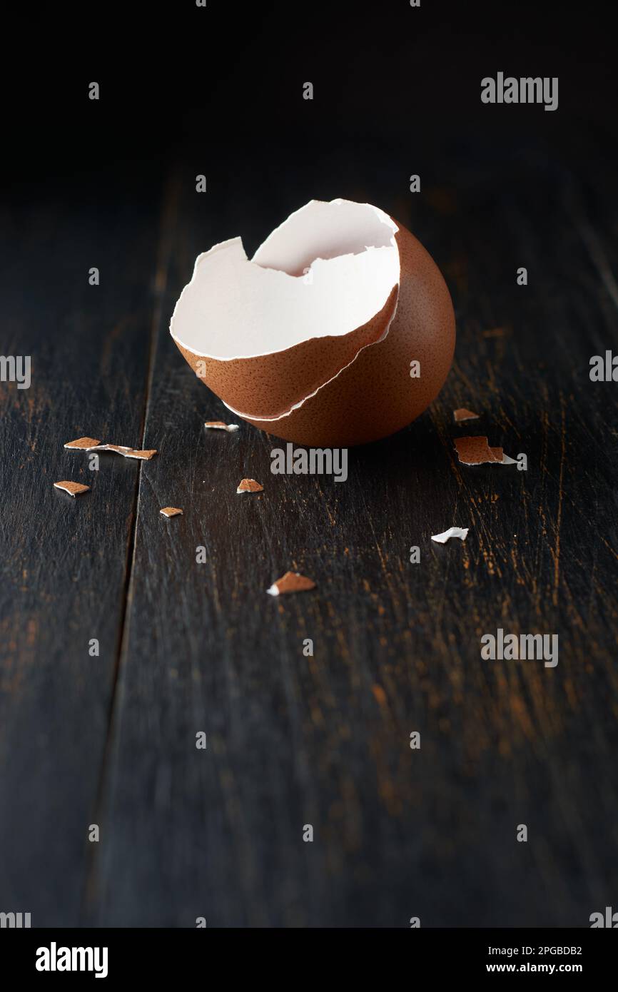 coquille d'œuf brun cassée ou fissurée avec des morceaux éparpillés sur la surface, isolée sur la surface de table noire rustique avec un fond flou Banque D'Images