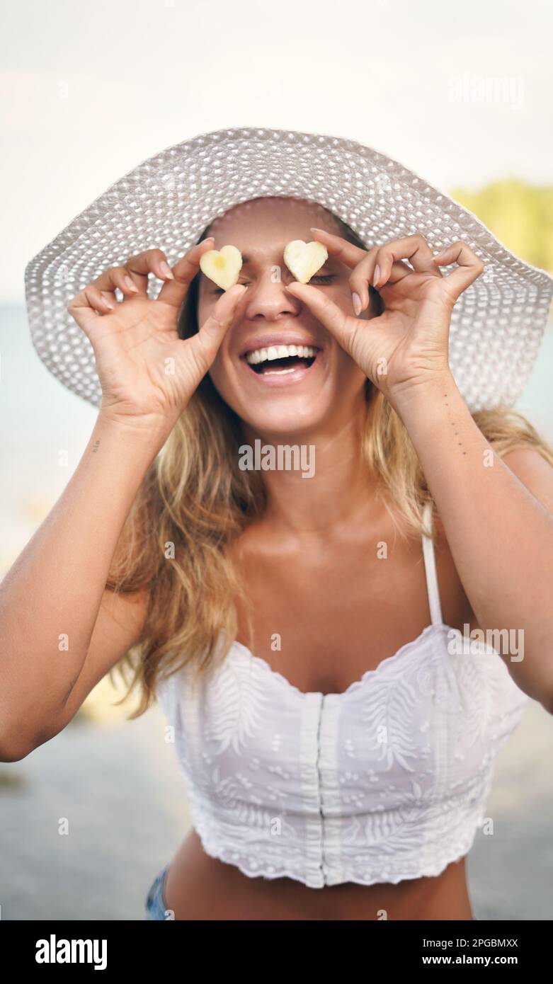 Un peu d'amour pour la vitamine C. une jeune femme attrayante debout seule et joueuse tenant des morceaux d'ananas en forme de coeur contre ses yeux. Banque D'Images