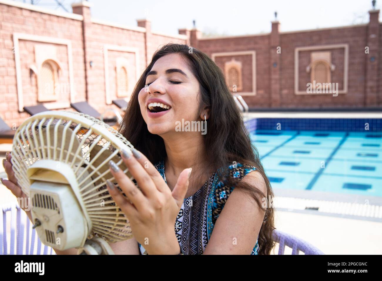 Jeune femme indienne appréciant le flux d'air du ventilateur électrique et refroidissant son corps à l'extérieur par jour ensoleillé. Chaleur estivale. Banque D'Images