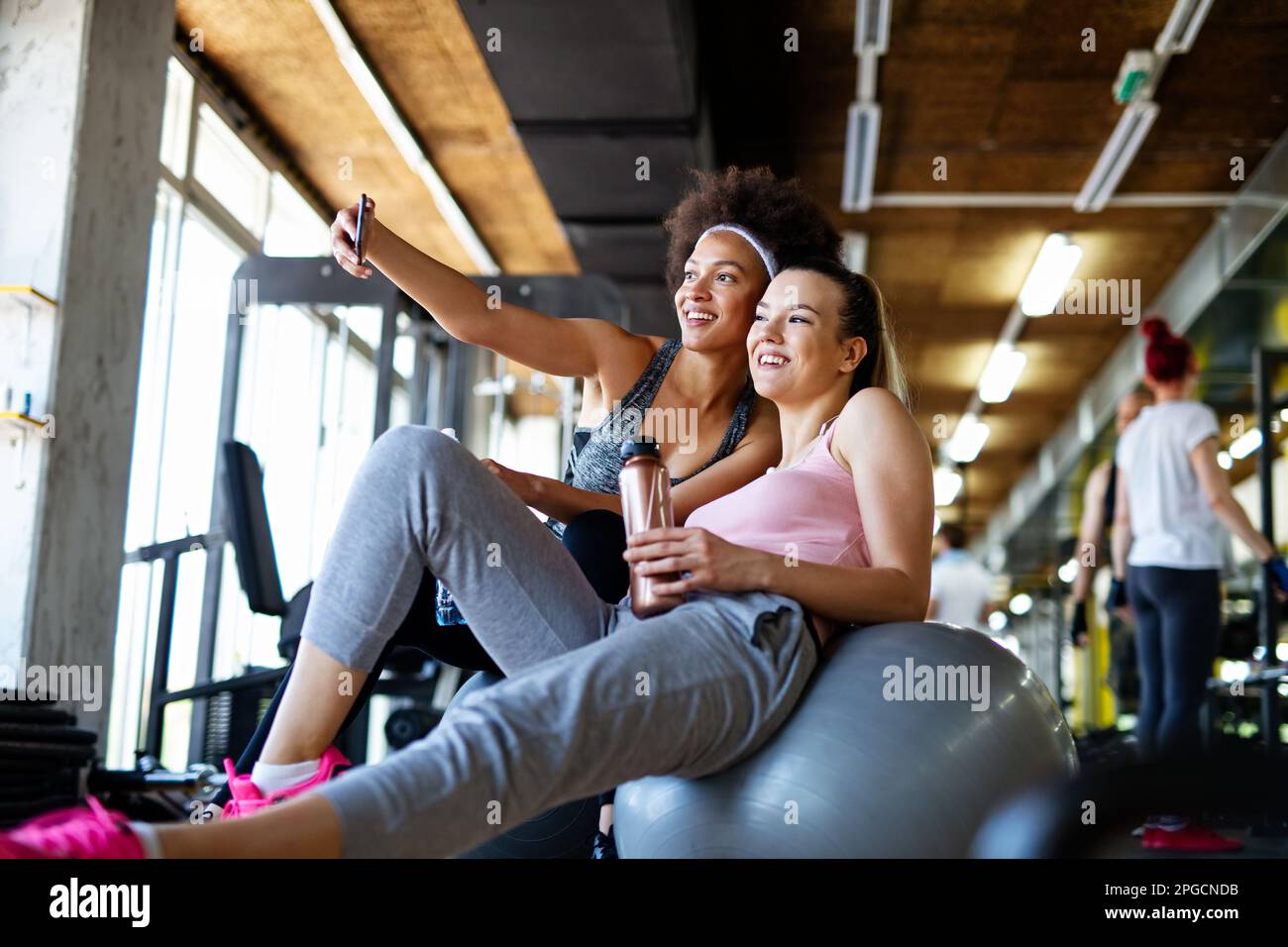 Des femmes en forme, des amis souriant, parlant et prenant des photos après l'entraînement dans la salle de gym. Médias sociaux. Banque D'Images