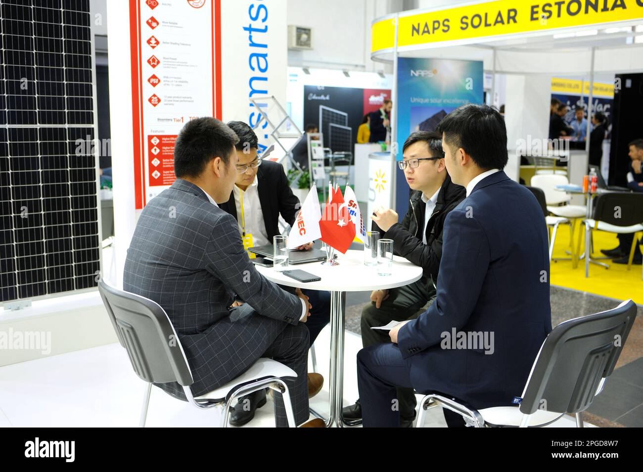 Engager le dialogue. Hommes d'affaires asiatiques assis à la table dans la zone du stand et négociant lors d'une exposition Solar Energy Trade Show. 19 avril, Banque D'Images