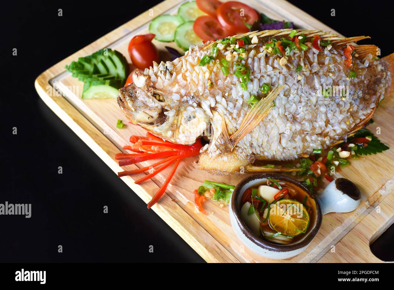 Perchaude grillée en pâte avec légumes et légumes verts sur un tableau de hachage en bois isolé sur fond noir vue latérale Banque D'Images
