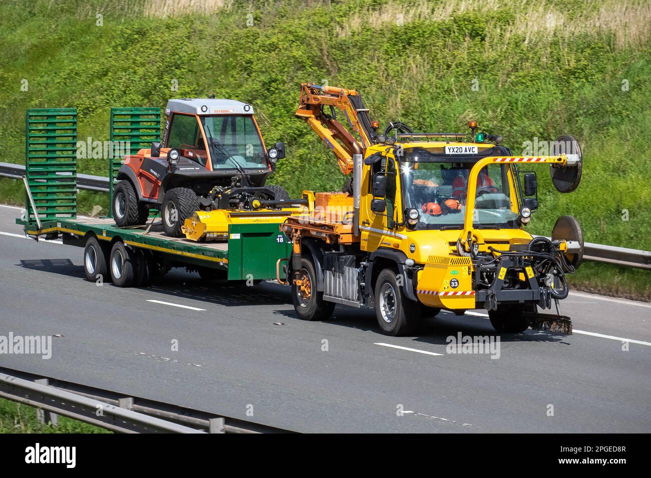 2020 jaune Mercedes-Benz UNIMOG, Diesel 3150 cc, corps RIGIDE à 2 ESSIEUX avec HIAB, et Reform Werke Metrac H 7 RX sur une remorque sur l'autoroute M6, Royaume-Uni Banque D'Images