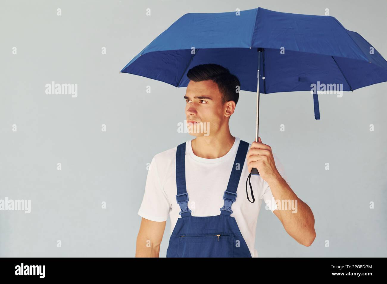 Tient le parapluie à la main. Homme en uniforme bleu debout à l'intérieur  du studio sur fond blanc Photo Stock - Alamy