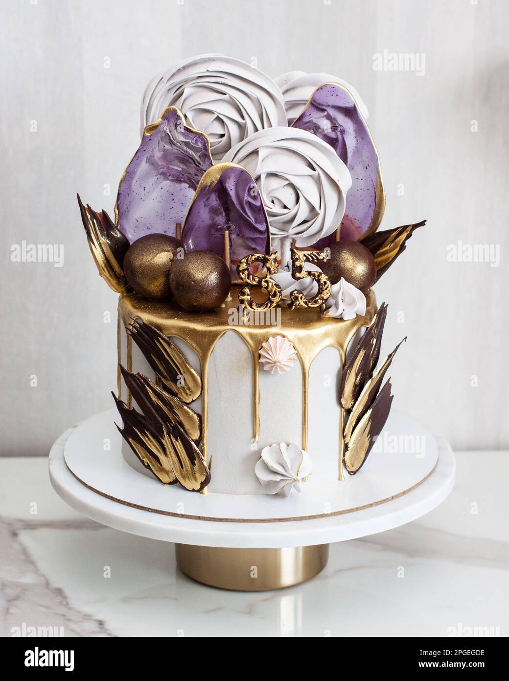 Gâteau rose tendre décoré de chocolat blanc fondu, macarons, meringues, pâtes à gâteau et bonbons sur cakestan blanc. Arrière-plan gris. Banque D'Images