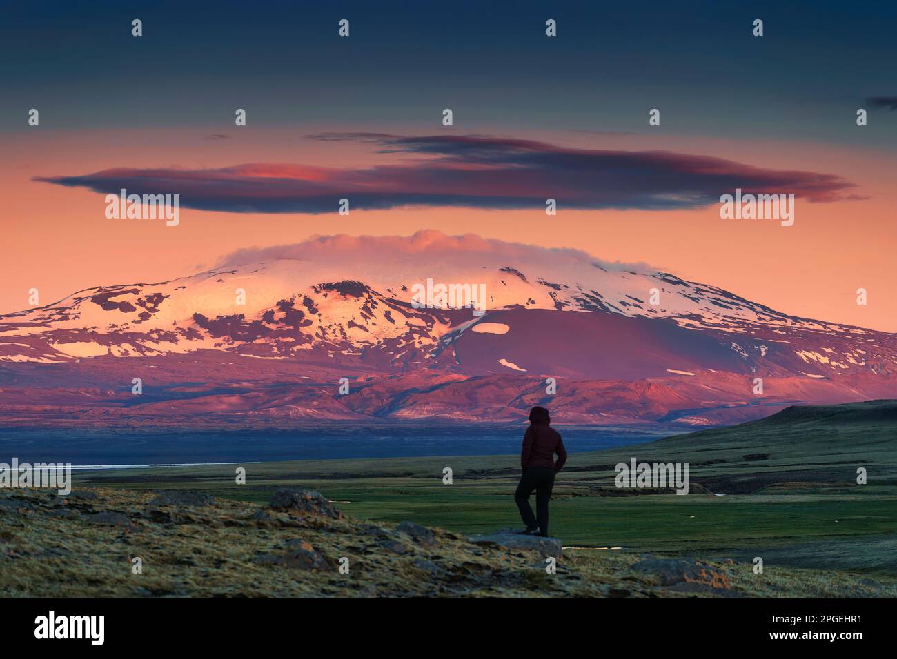 Jeune aventurier féminin debout sur un champ de lave et une majestueuse montagne volcanique avec un ciel coloré au crépuscule dans une nature sauvage éloignée en été à Highl Banque D'Images