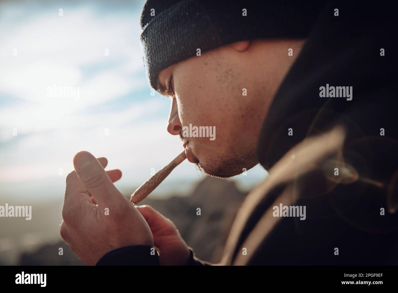 Garçon fumant un joint de marijuana sur une montagne au coucher du soleil Banque D'Images