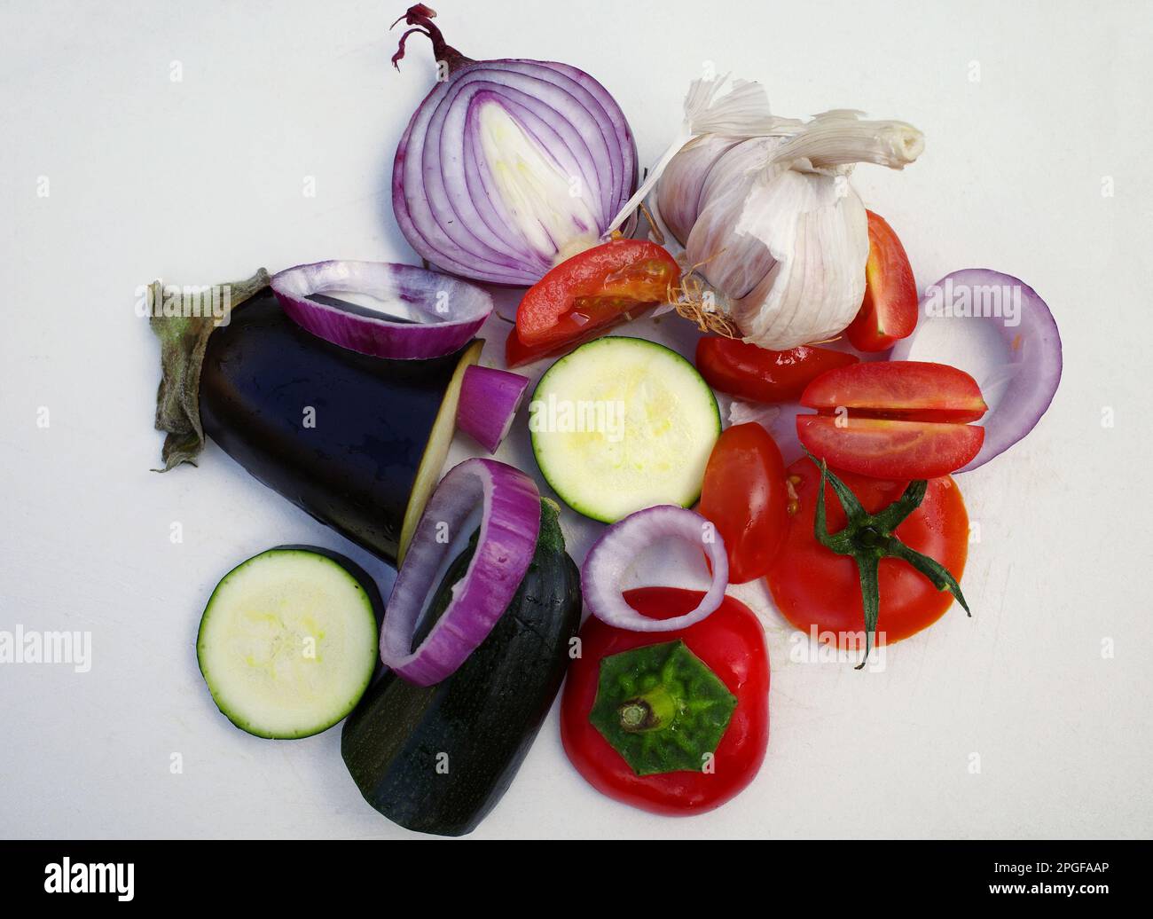 Légumes mélangés pour un plat méditerranéen sur une planche à découper blanche. Les oignons rouges, les courgettes, les aubergines, l'ail, les tomates et le poivron sont sur l'assiette Banque D'Images
