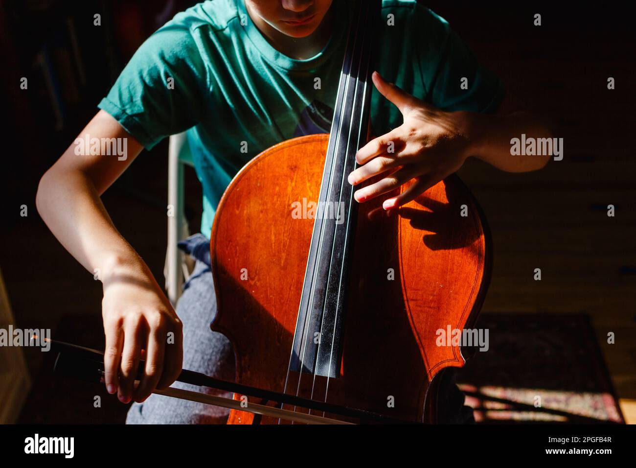 Gros plan d'un garçon assis dans une zone lumineuse de violoncelle pratiquant la lumière Banque D'Images