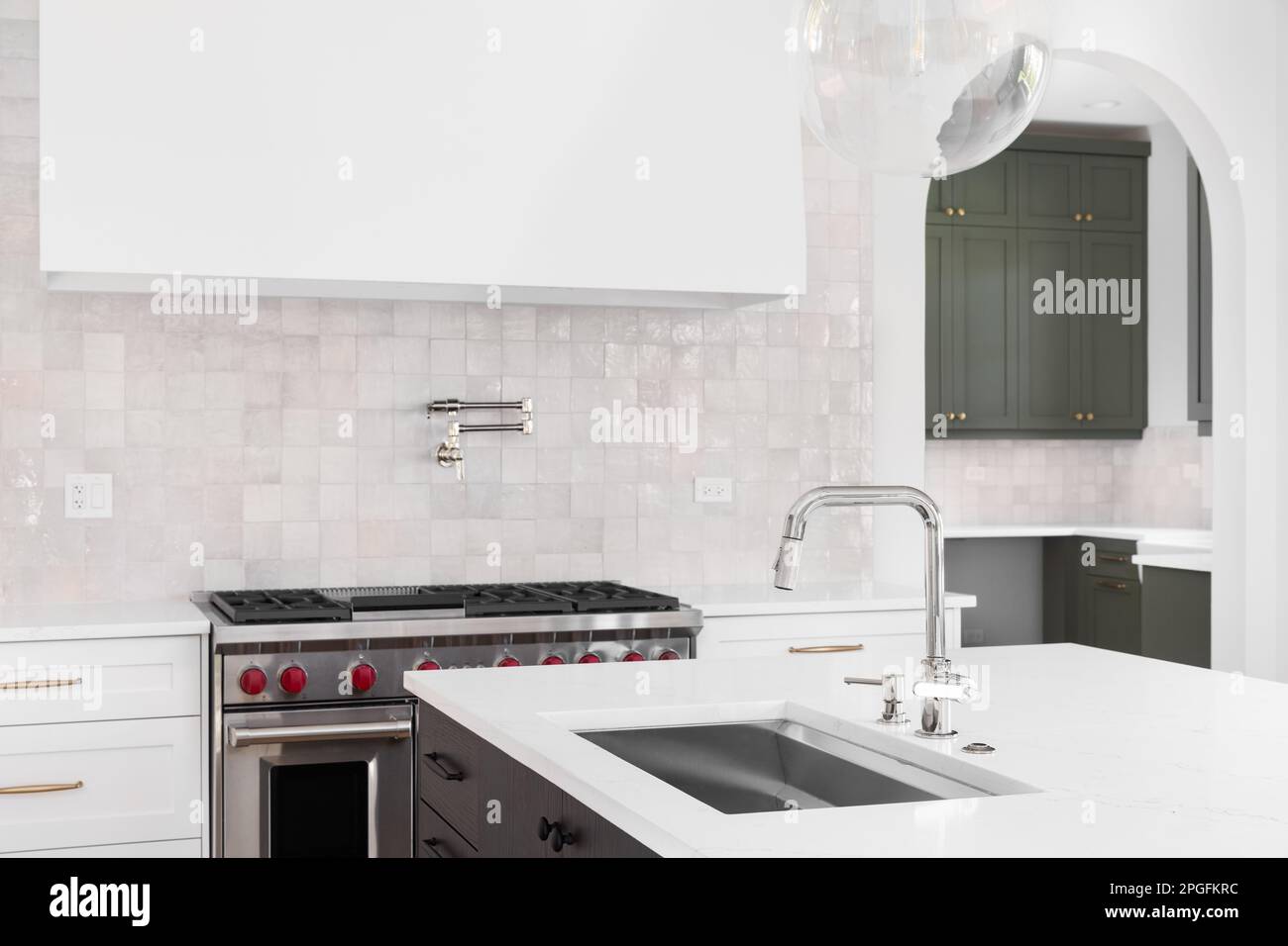 Un détail de cuisine avec un évier sur le comptoir en marbre d'une île avec une cuisinière, une hotte, et une dosseret de carrelage en arrière-plan. Banque D'Images