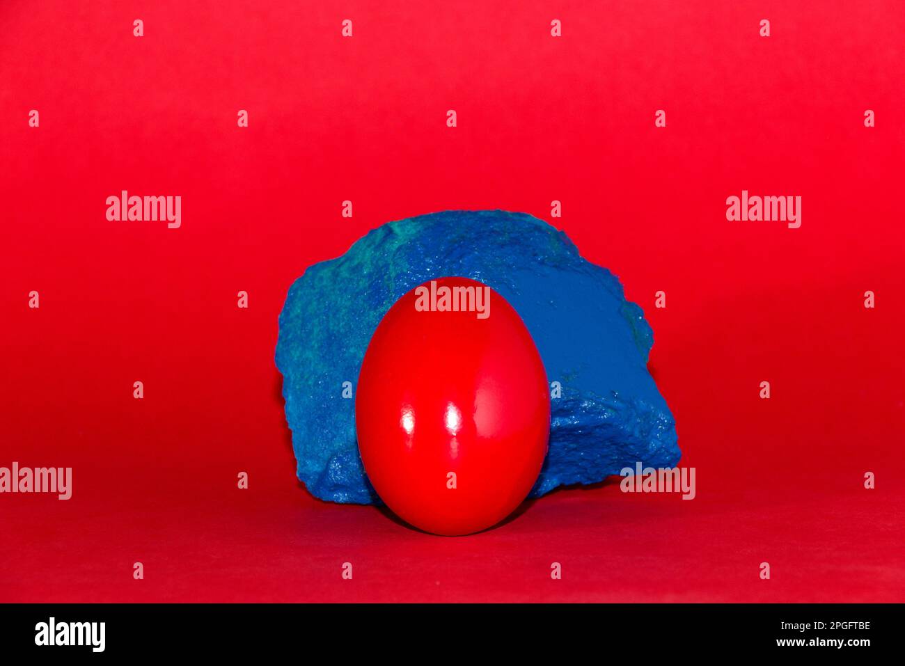 Œuf de Pâques rouge reposant sur le rocher bleu, fond rouge, design de vacances créatif Banque D'Images