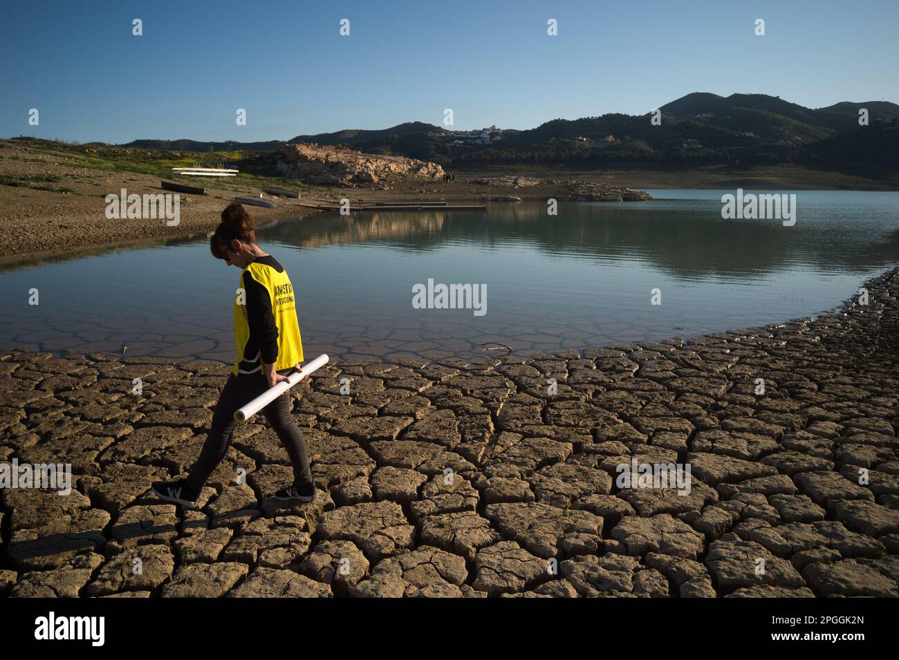 Un militant des droits de l'homme est vu marcher sur un terrain fissuré après une manifestation contre le changement climatique, organisée par Amnesty International. Pour marquer la Journée internationale de l'eau, des militants d'Amnesty International, ainsi que plusieurs organisations environnementales, ont dénoncé le changement climatique et ses effets sur les droits de l'homme dans le monde entier par une performance qui représente la mort symbolique du réservoir de la Viñuela. Le réservoir de Viñuela, qui fournit de l'eau aux municipalités près de la région d'Axarquia, est à un niveau d'eau minimal en raison de la grave sécheresse dans la province. Banque D'Images