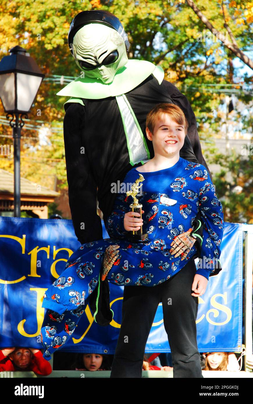 Un jeune enfant présente son trophée lors d'un concours de costumes d'Halloween, représentant un étranger transportant un enfant Banque D'Images
