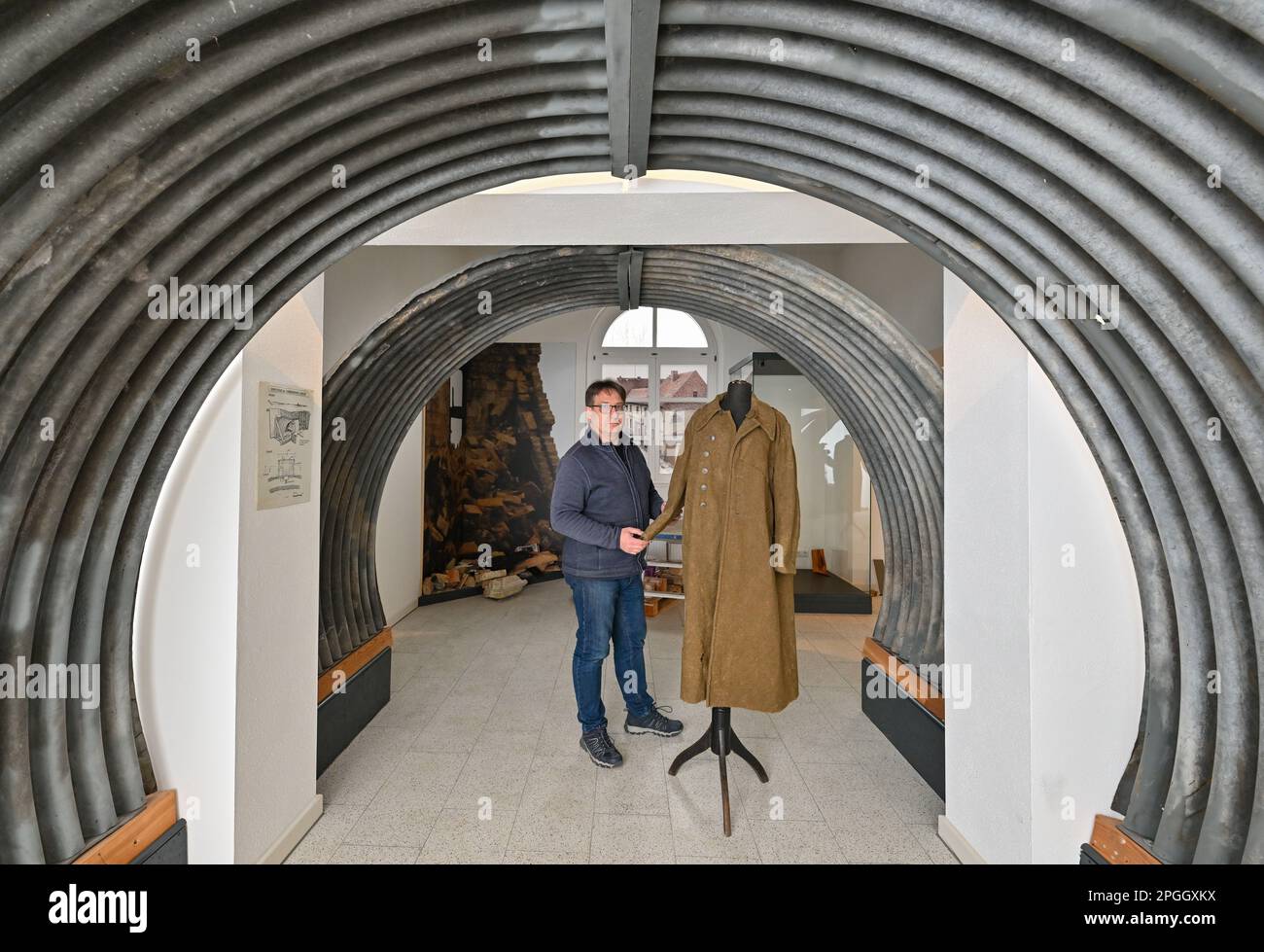 21 mars 2023, Brandebourg, Seelow: Thomas Drewing, président de la Société d'histoire historique et locale de Gusow-Platkow (Märkisch-Oderland), se dresse dans le bâtiment de la gare de Seelow dans le nouveau 'Seelow/Mark History Station' sous des feuilles ondulées d'anciens bunkers à côté d'un manteau d'un rapatrié d'un camp de prisonniers de guerre. Comment les habitants, les réfugiés et les soldats ont-ils vécu les années d'avant-guerre, de guerre et d'après-guerre dans la région de l'Oder? Les réponses à ces questions sont maintenant fournies par la « station d'histoire de Seelow/Mark » dans l'ancienne gare - compilée et conçue par le bénévole historique Pec Banque D'Images