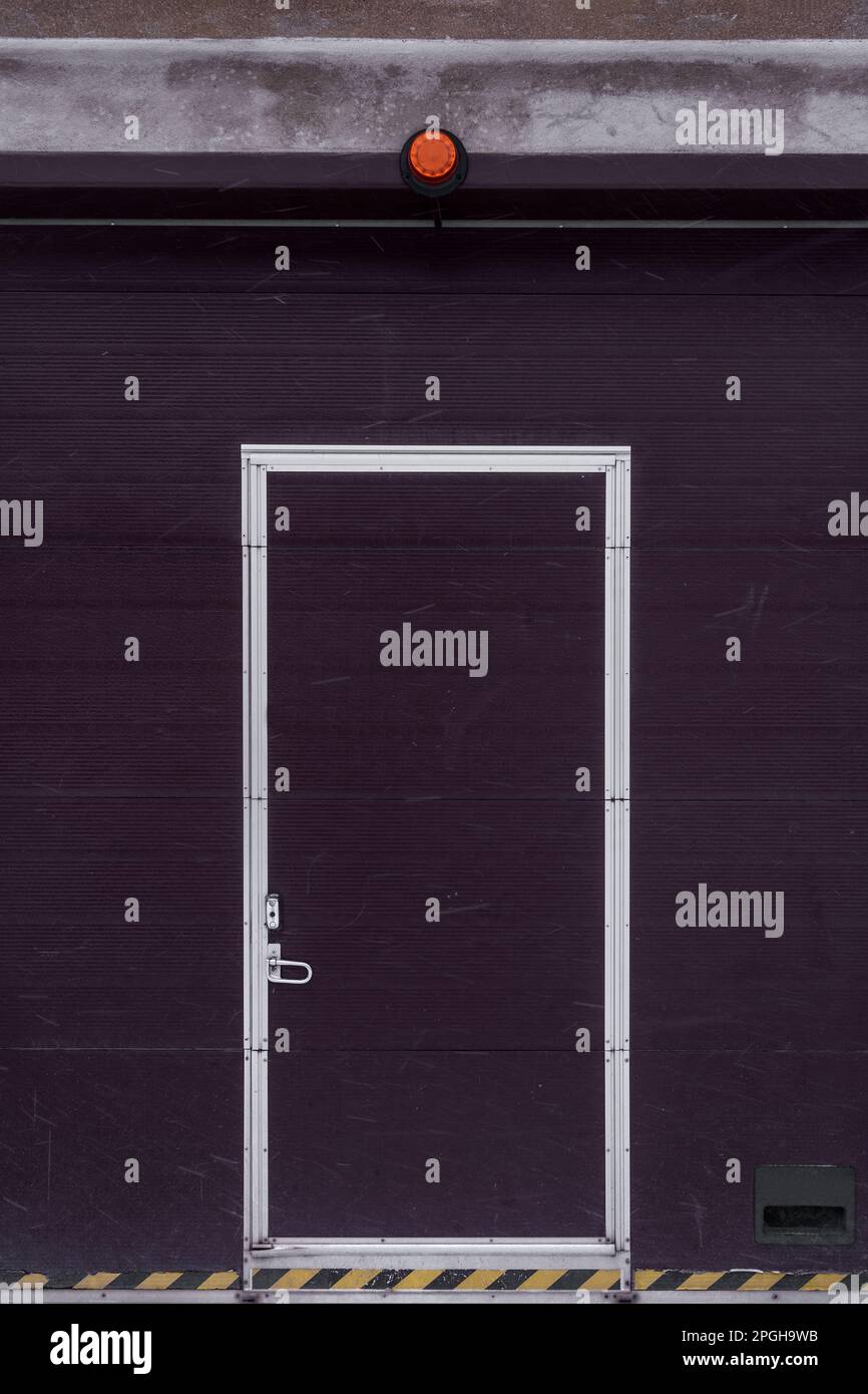 Porte de garage industrielle avec porte de passage et voyant d'alerte rouge en hiver. Banque D'Images