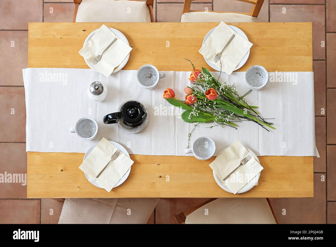 Préparation pour une pause-café de l'après-midi avec quatre assiettes, tasses, serviettes, cafetière et fleurs de tulipe sur une table blanche sur une table en bois, Top vie Banque D'Images