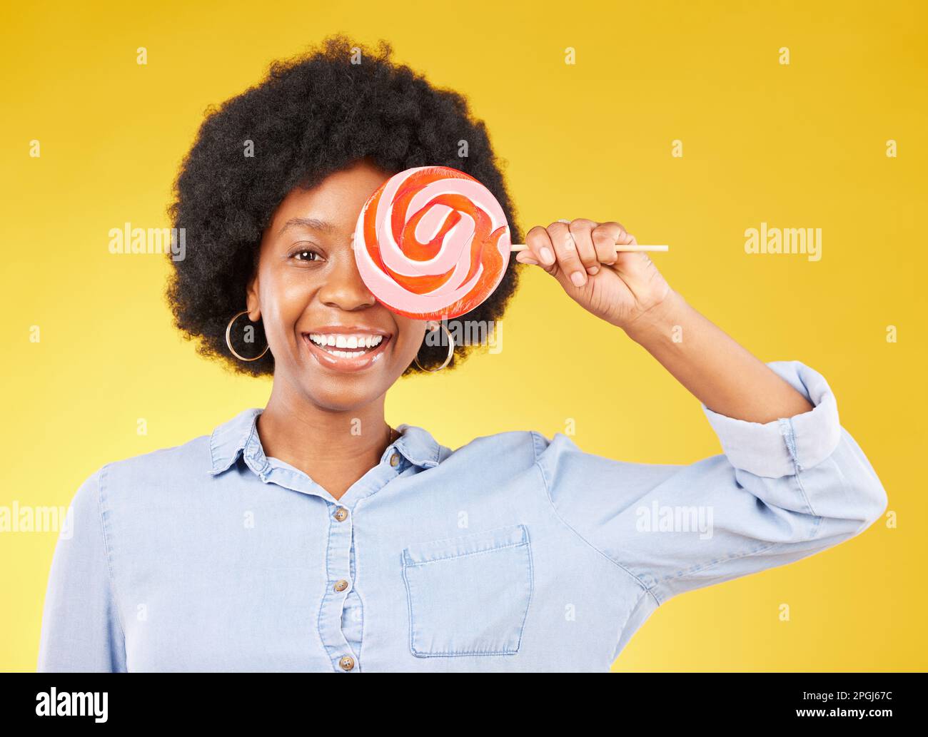 Couverture, bonbons et lipop avec femme noire en studio pour coloré, gai et positif. Jeune, bonheur et dessert avec femelle isolée sur jaune Banque D'Images