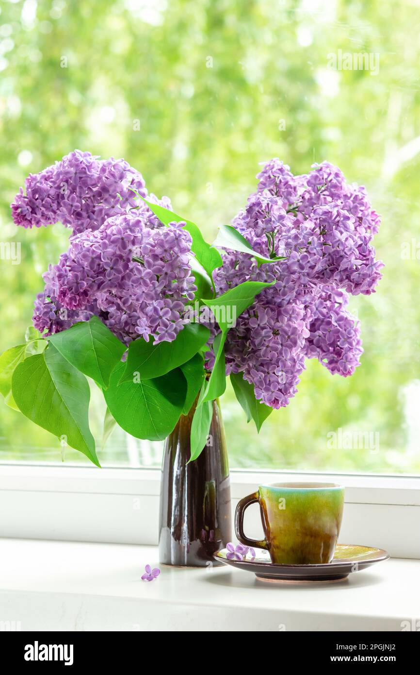 Intérieur avec un bouquet de fleurs de lilas sur la fenêtre. Thé le matin du printemps dans la cuisine près de la fenêtre Banque D'Images