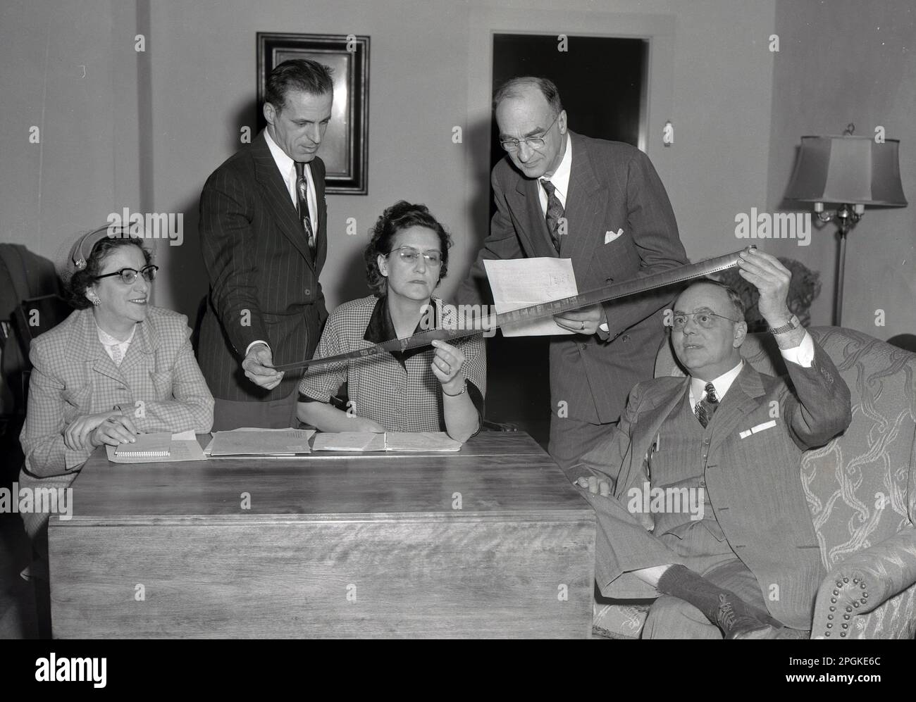 1950s, historique, plusieurs hommes et femmes bien habillés à l'intérieur d'un salon, regardant une bande de 35mm négatifs de film, Etats-Unis. Banque D'Images