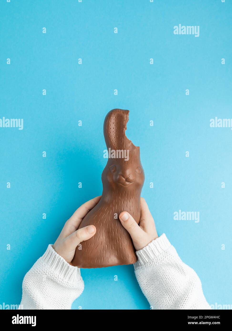 Mains de l'enfant tenant le lapin de Pâques au chocolat avec les oreilles mordues sur fond bleu, concept de famille. Verticale, vue de dessus Banque D'Images