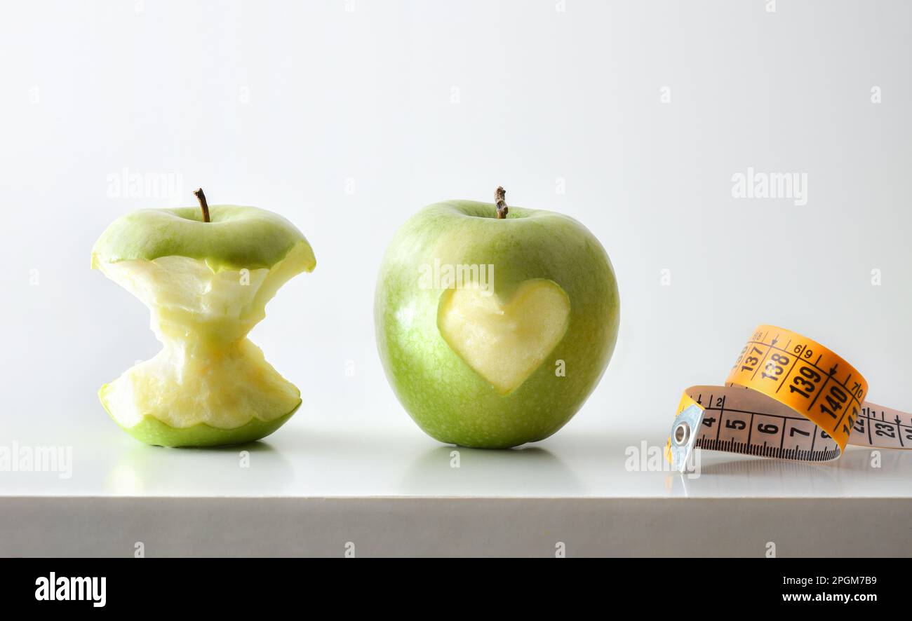Concept de saine alimentation et de contrôle du corps avec pomme avec coeur et moitié mangé pomme et mètre ruban sur table blanche et fond blanc isolé. F Banque D'Images
