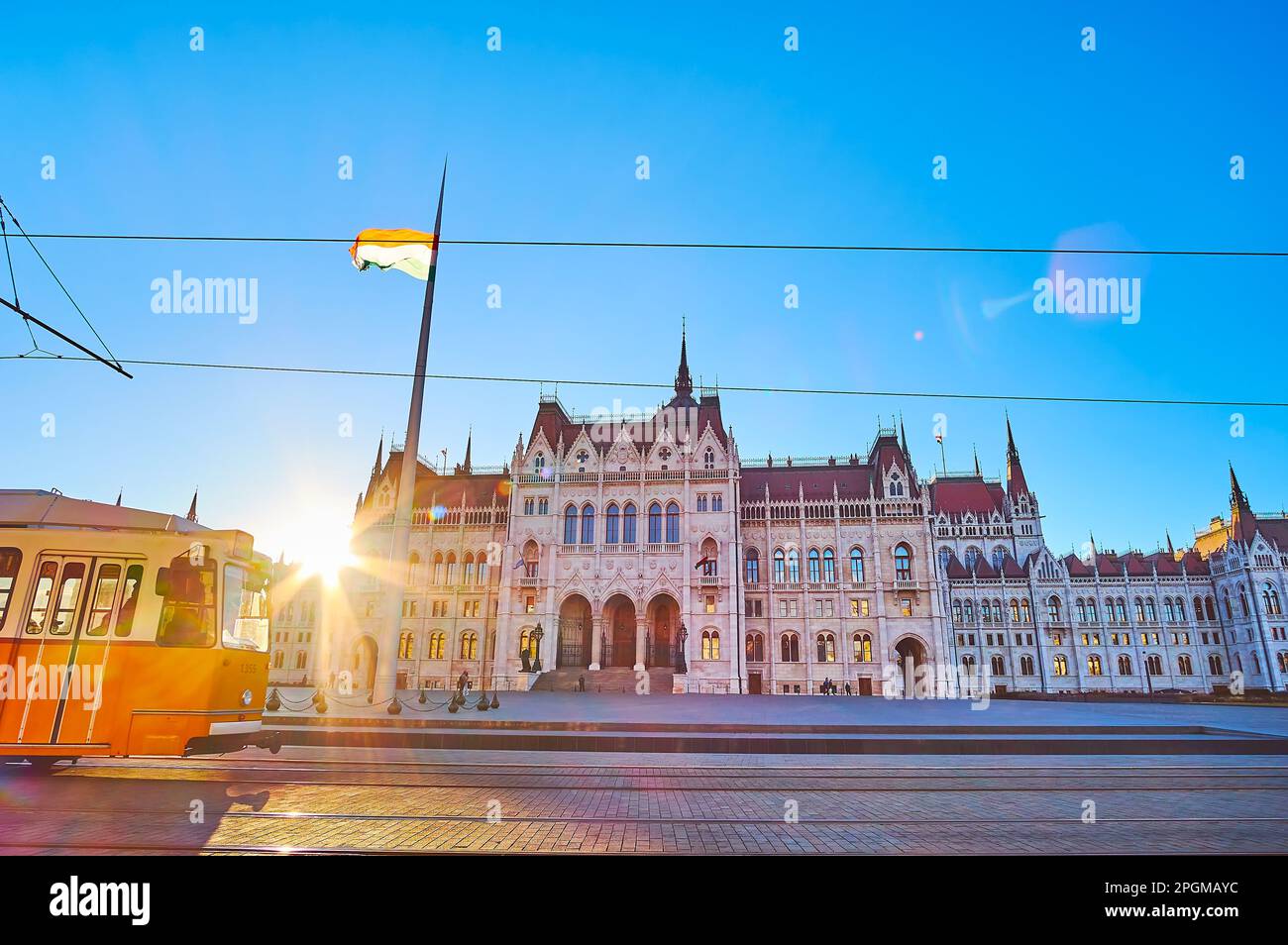 Le coucher de soleil lumineux derrière le Parlement gothique très orné sur la place Lajos Kossuth avec le tramway jaune en premier plan, Budapest, Hongrie Banque D'Images