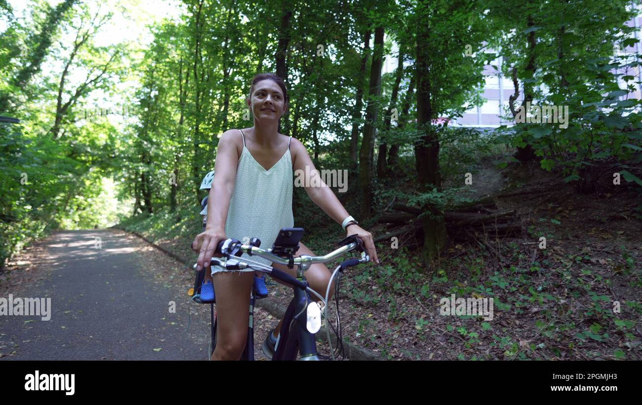 Mère à vélo avec enfant dans un siège de vélo sur un sentier vert à l'extérieur. Voyage d'activités en famille et le week-end Banque D'Images