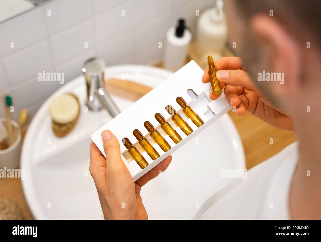 Mains de sexe masculin tenant des ampoules cosmétiques avec du sérum pour la croissance des cheveux, la restauration des cheveux de beauté dans une salle de bains moderne et lumineuse. Concept de perte de cheveux et de problème Banque D'Images