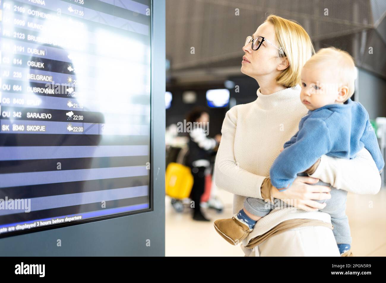 Mère voyageant avec un enfant, tenant son bébé garçon au terminal de l'aéroport, vérifiant l'horaire des vols, attendant de monter à bord d'un avion. Concept voyage avec enfants Banque D'Images